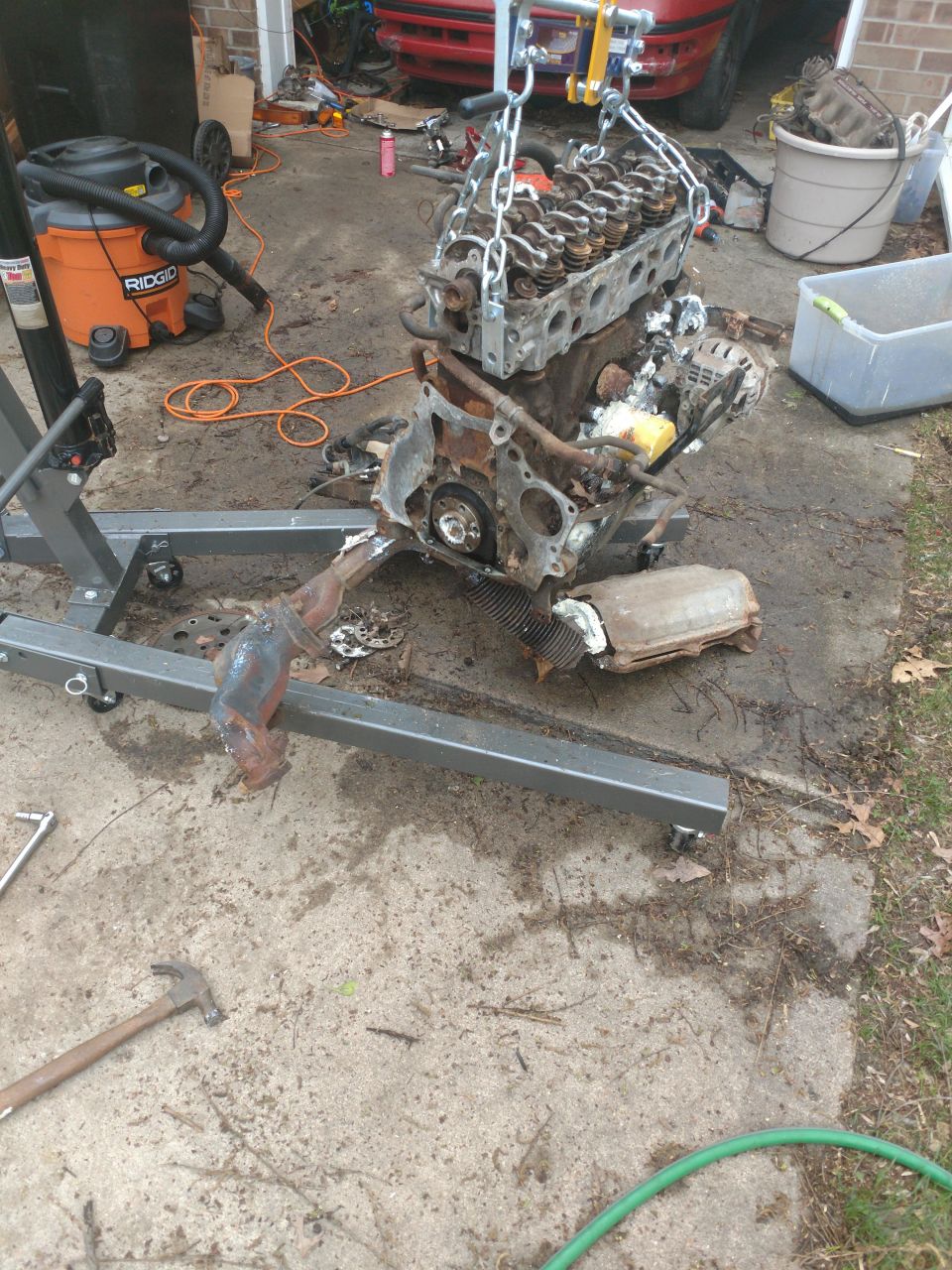 Disassembled engine on hoist, shop vacuum, tools, concrete driveway