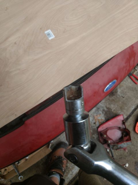 1989 Ford Probe - A close-up shot shows a socket wrench with a socket attached, positioned over a red car body panel. A wooden surface is visible in the back…