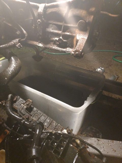 1989 Ford Probe - A heavily soiled engine or transmission component is being pressure washed, with the runoff collecting in a large plastic tub below. A gree…