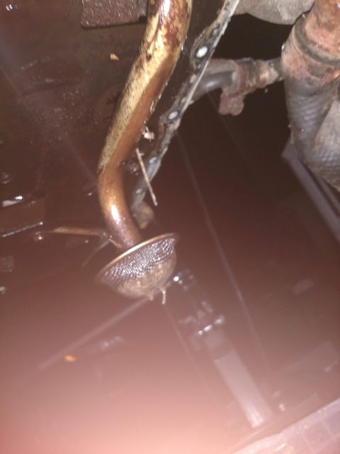 1989 Ford Probe - A close-up view shows the oil pickup tube and screen assembly from a vehicle's oil pan, coated in dark, viscous oil.