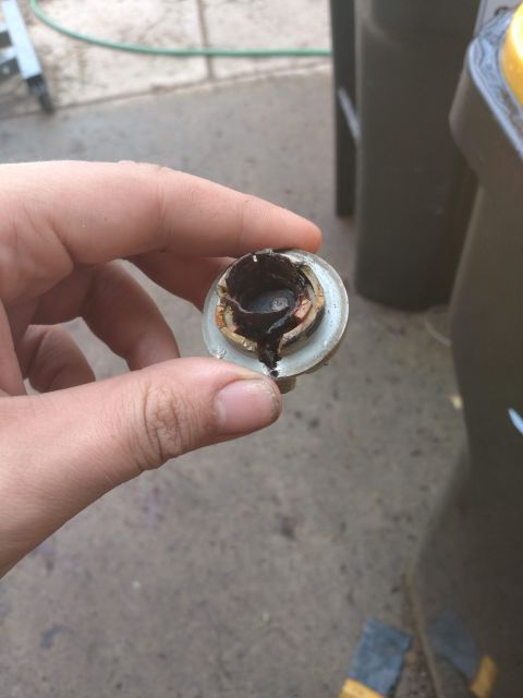 1989 Ford Probe - A hand holds a damaged, burnt-out light bulb socket with visible corrosion and melted plastic. The background shows a concrete surface and…