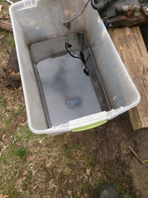 1989 Ford Probe - A clear plastic tub contains dark liquid, possibly used oil, with a rainbow sheen on the surface. A black electrical cord is submerged in t…