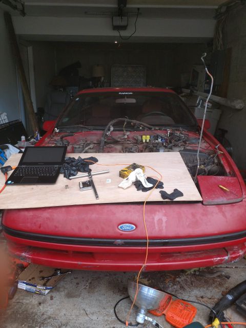 1989 Ford Probe - A red Ford Probe is parked in a garage with its hood open, revealing disassembled engine components. A laptop and tools are laid out on a w…
