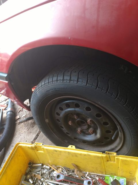 1989 Ford Probe - A close-up view of the rear wheel well of a red car, showing the tire, rim, and lug nuts. A yellow toolbox filled with various tools is in…