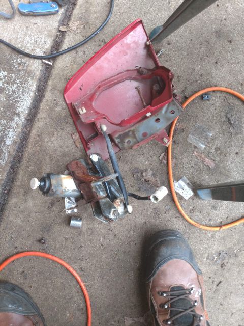 1989 Ford Probe - A disassembled red car part, likely a taillight housing, is laid out on a concrete surface next to a rusty mechanism and an orange cord. Th…