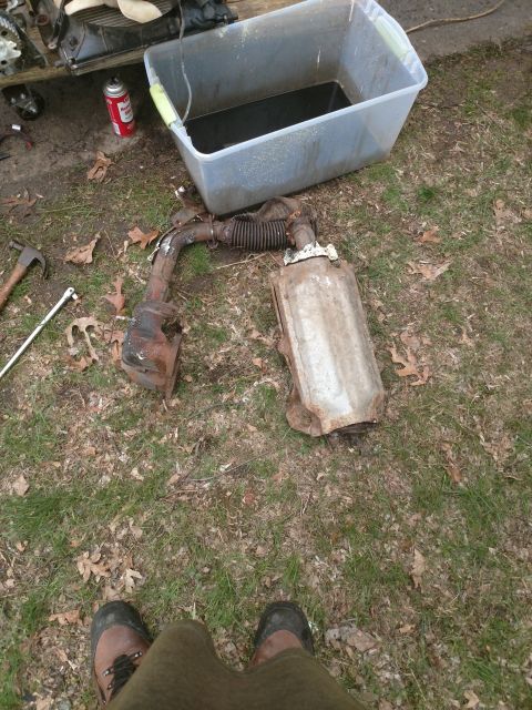 1989 Ford Probe - A removed exhaust system, including a catalytic converter and muffler, lies on the ground next to a plastic tub filled with dark liquid. A…