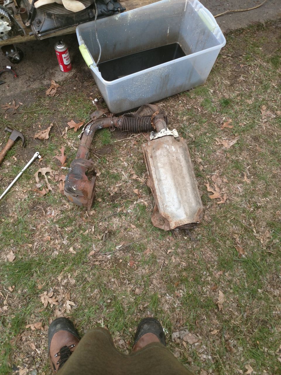 Removed car exhaust system and a tub of fluid on the ground.