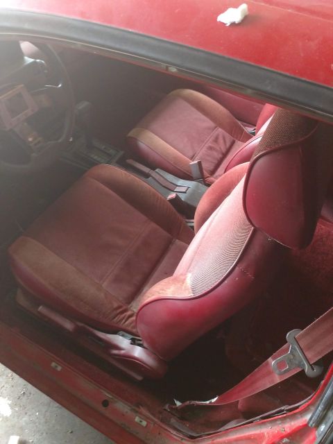 1989 Ford Probe - The interior of a red car shows the driver's seat and passenger seat, both upholstered in a reddish-brown fabric. The dashboard and steerin…