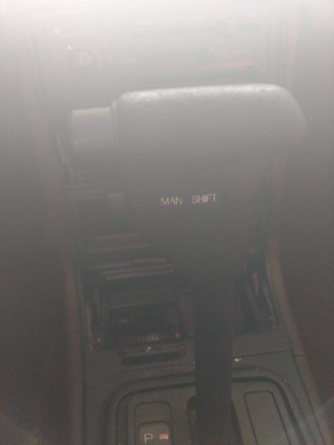 1989 Ford Probe - A close-up interior shot shows the automatic gear shifter of a car. The shifter has "MAN SHIFT" printed on it, indicating a manual shifting…