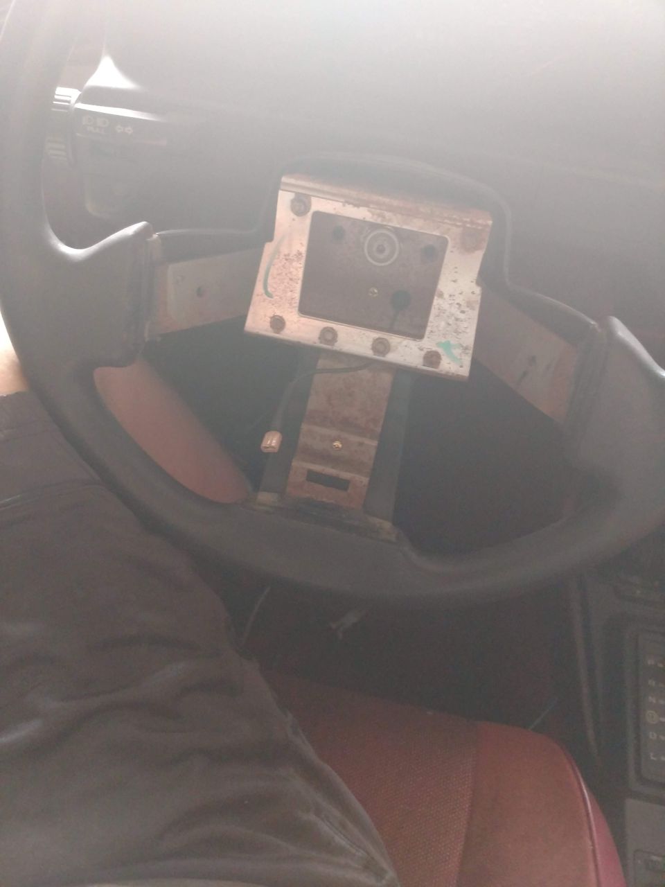 Car steering column with steering wheel removed, showing mounting bracket and dashboard.