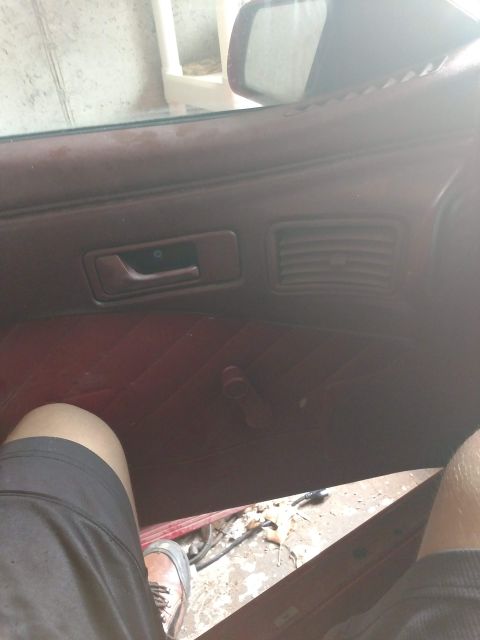 1989 Ford Probe - The interior of a car door panel is shown, featuring a maroon color, a manual window crank, and a door handle. A person's legs are visible…