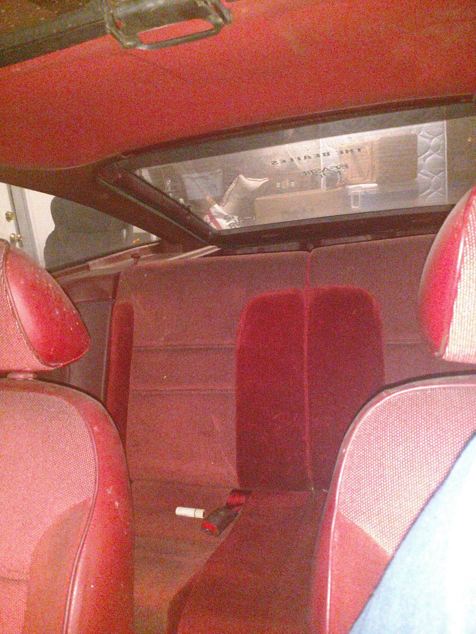 Interior of a vintage car with red seats and a sign reading "THE BEATLES" visible through the rear window.