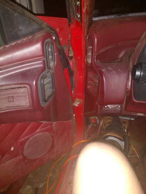 1989 Ford Probe - The interior of a red vehicle shows the driver's side door panel and dashboard. A person's leg and foot wearing a brown boot are visible ne…