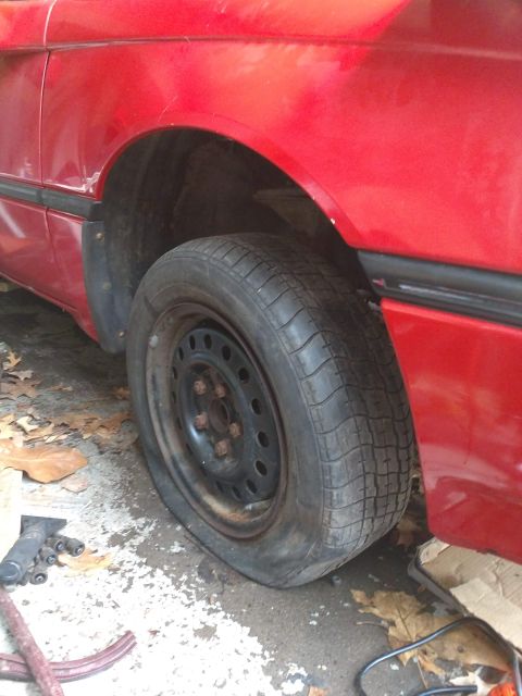 1989 Ford Probe - A close-up view of a flat tire on a red car. The tire is completely deflated and resting on the rim, with the car's fender visible above it.