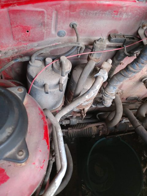1989 Ford Probe - A close-up view of the engine bay of a red vehicle, showing various hoses, filters, and wiring. A VIN number is visible stamped on the red…