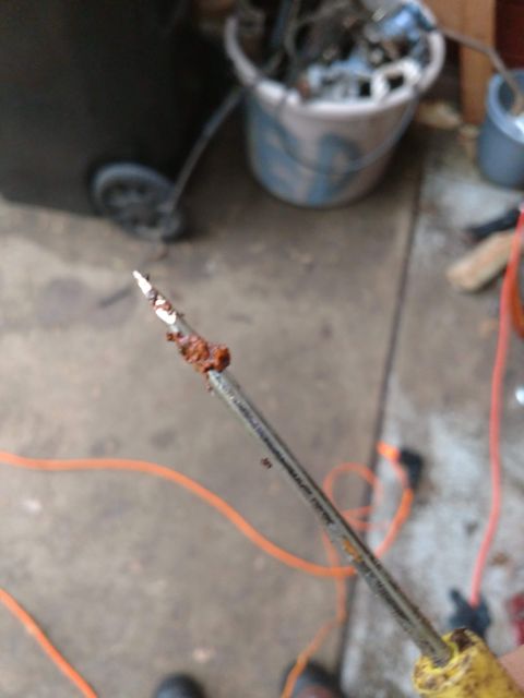1989 Ford Probe - A close-up shot of a rusty screwdriver with some debris on its tip. In the background, a blurry scene shows a bucket and some orange cords.