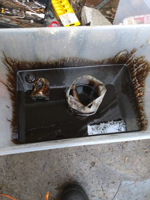 1989 Ford Probe - A drain pan filled with dark, used motor oil. A used oil filter and a small metal part are submerged in the oil. Tools and debris are visib…