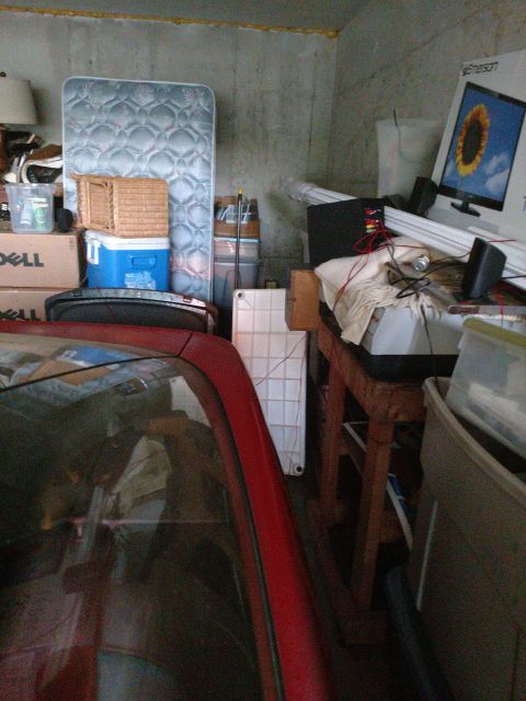 1989 Ford Probe - A red vehicle is partially visible in the foreground, reflecting items stored in a garage. The background shows a mattress, a cooler, boxes…