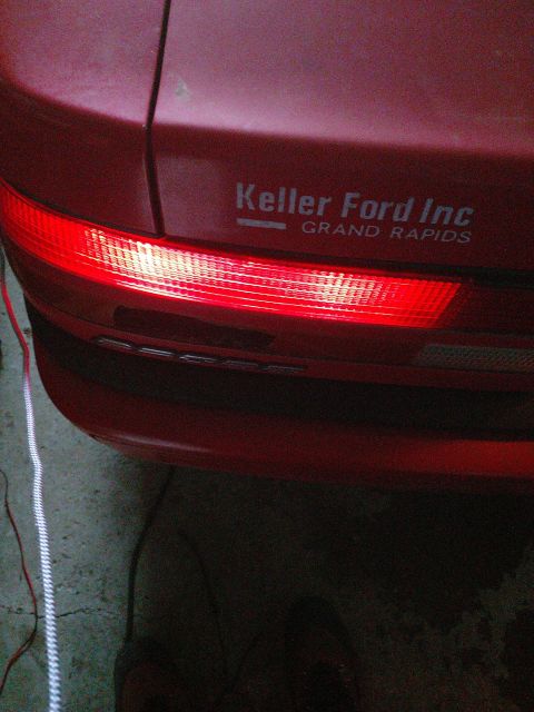 1989 Ford Probe - The rear of a red car is shown, featuring a lit taillight and a decal that reads "Keller Ford Inc GRAND RAPIDS".