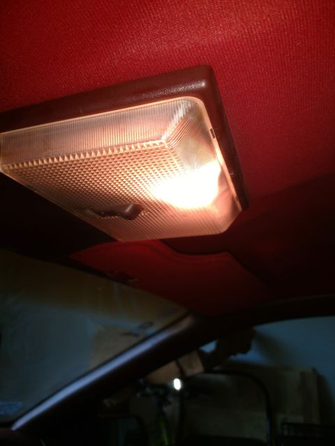 1989 Ford Probe - A close-up view of a car's interior dome light, illuminated against a red headliner. The light fixture has a textured plastic cover and a b…