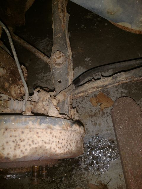 1989 Ford Probe - This is a close-up, low-angle shot of heavily rusted suspension components and a brake drum assembly, likely from the undercarriage of a ve…