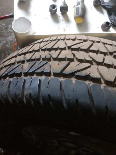 1989 Ford Probe - A close-up, low-angle shot of a dirty tire with a distinct tread pattern. The background shows a white surface with various tools and parts…