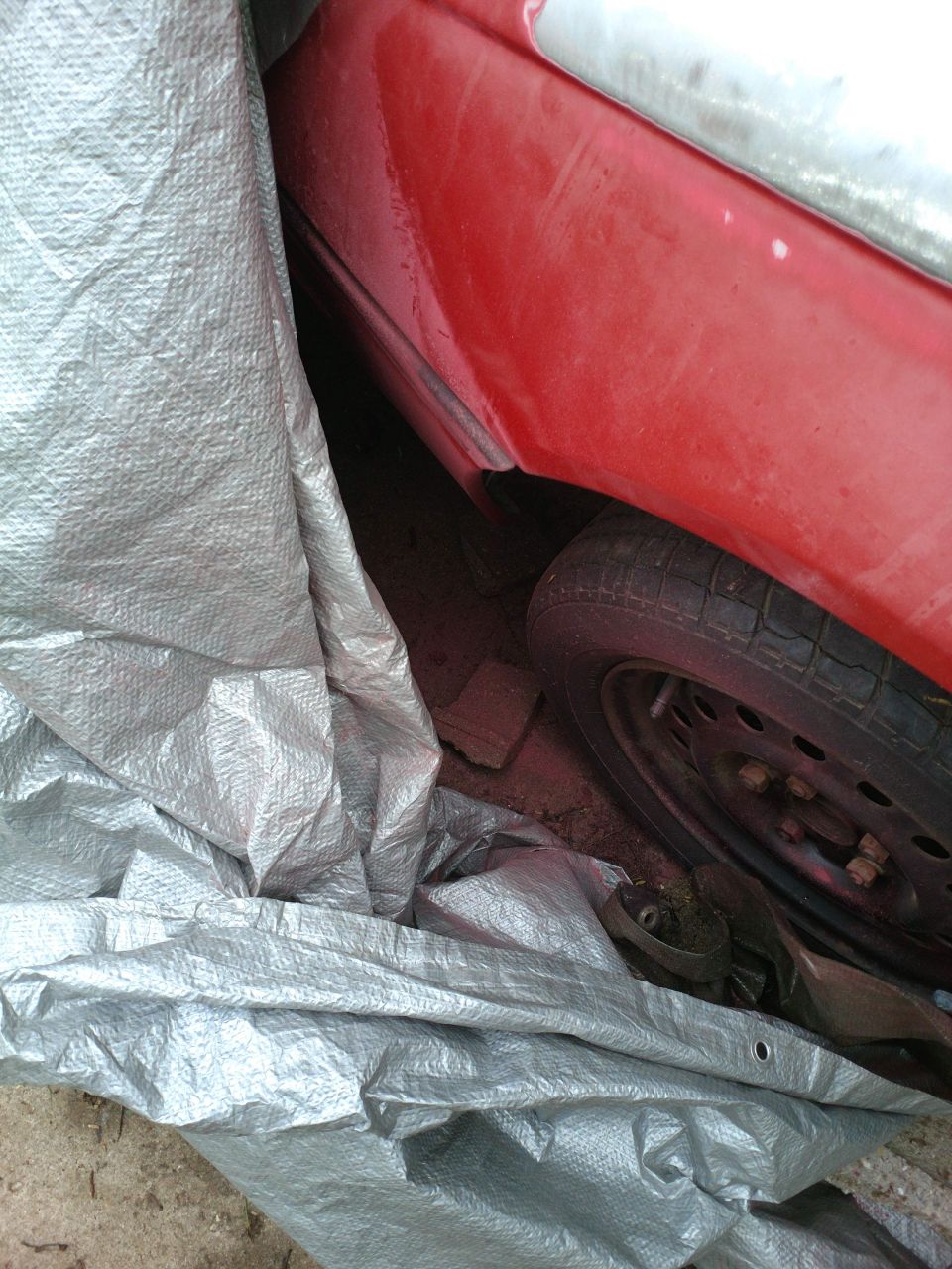 Red car fender and tire under a silver tarp.
