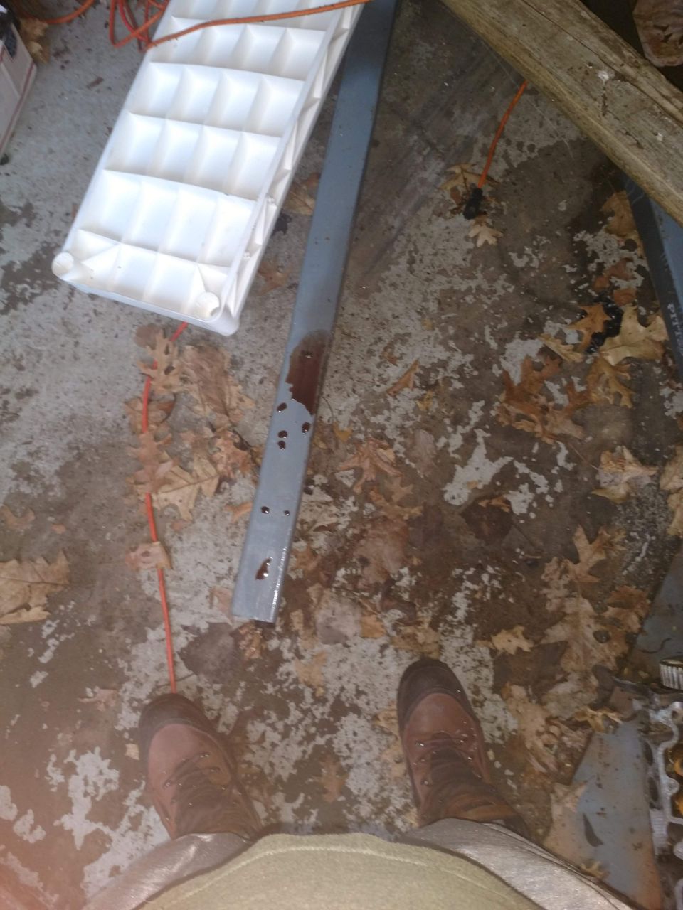 Person in boots on leaf-covered concrete with ice tray and metal bar