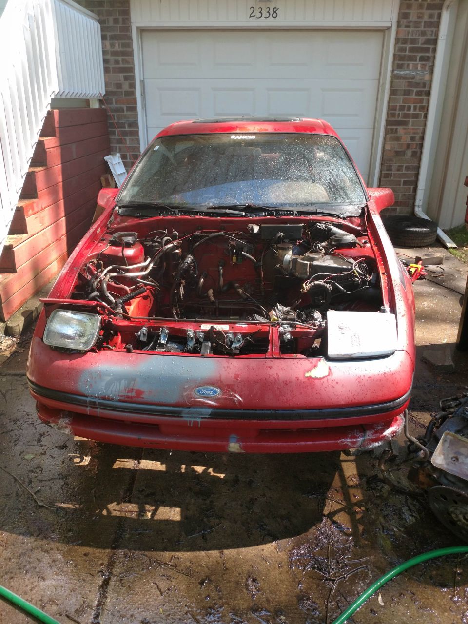 Red 1989 Ford Probe with hood open, parked on a wet driveway.