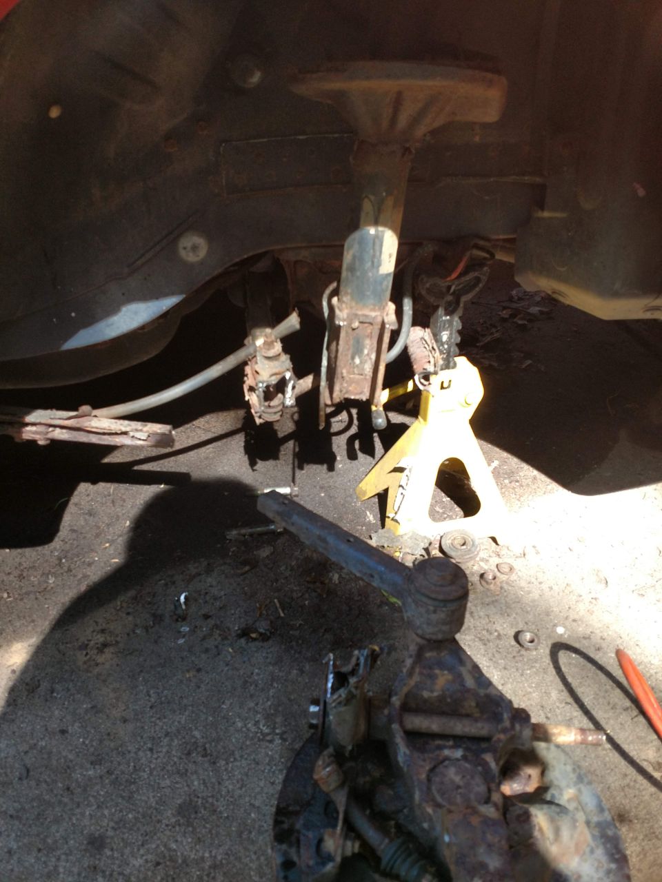 Close-up of rusty car suspension components with a yellow jack stand.