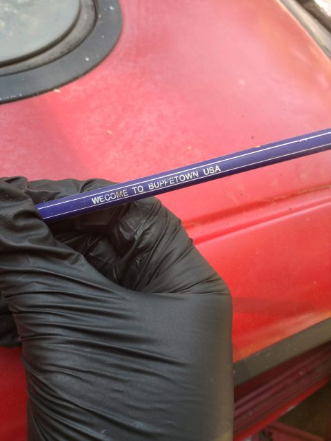1989 Ford Probe - A gloved hand holds a purple pencil with white text that reads "WECOME TO BUPPETOWN USA" against a red vehicle surface.