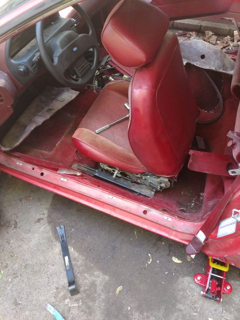 1989 Ford Probe - The interior of a red car is shown, with the driver's seat removed and the floor exposed. A steering wheel and dashboard are visible, along…