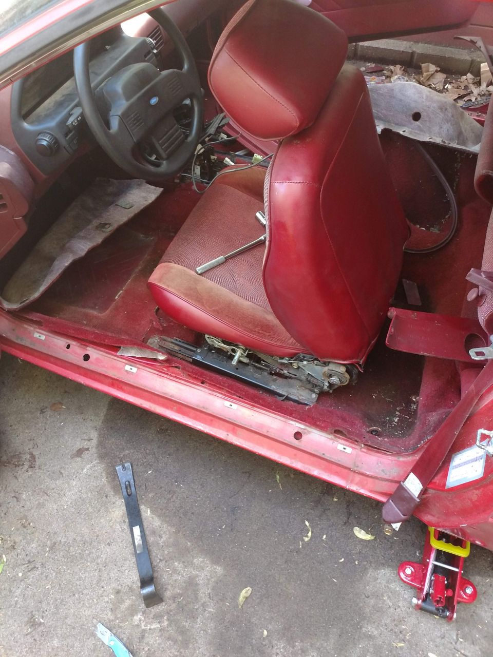 Interior of a red car with driver's seat removed, showing floor and dashboard.