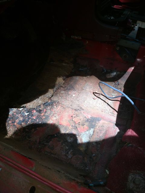 1989 Ford Probe - The interior floor of a vehicle shows significant rust and damage, with exposed metal and debris. A blue wire is visible running across the…