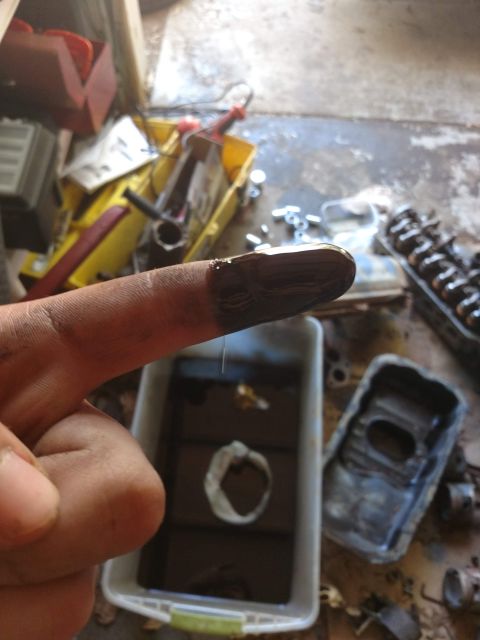 1989 Ford Probe - A close-up shot shows a finger covered in dark, oily residue, with a white plastic container filled with the same dark liquid in the backgr…