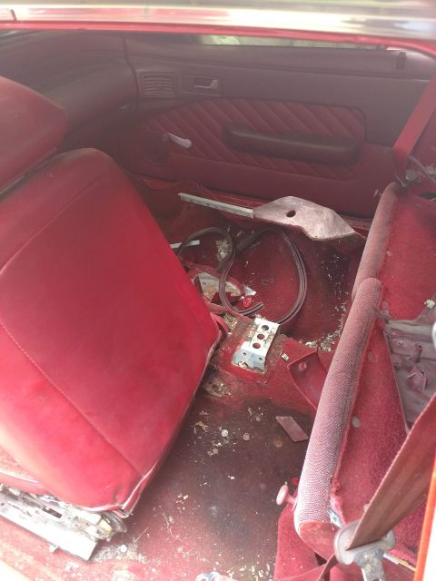 1989 Ford Probe - The interior of a red car shows a red seat and red carpeted floor with debris. The driver's side door panel is visible with a black armrest…