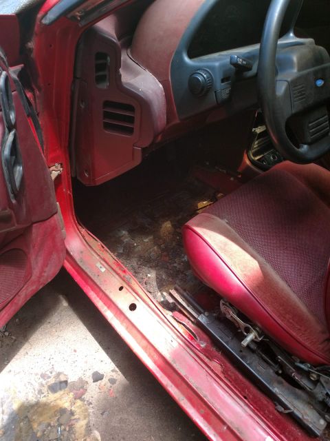 1989 Ford Probe - Interior view of a red 1989 Ford Probe, showing the driver's seat, dashboard, and door panel. The interior appears worn and dirty, with vis…