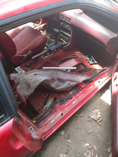 1989 Ford Probe - The interior of a red 1989 Ford Probe is shown from a high angle, looking down into the passenger side. The interior is heavily damaged and…