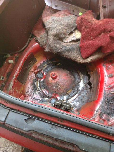 1989 Ford Probe - The interior of a red vehicle's trunk area shows significant rust and debris, with a spare tire well visible. A dark rubber seal runs along…