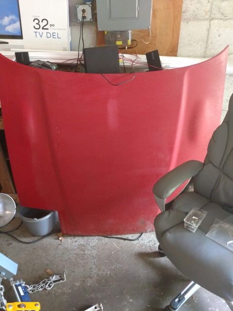 1989 Ford Probe - A red car hood is propped up against a wall in a garage. Various electronic equipment and a gray office chair are visible in the background.