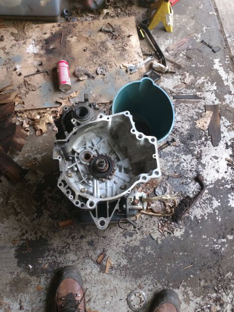 1989 Ford Probe - A disassembled car transmission sits on a dirty garage floor next to a teal funnel and a can of spray paint. The transmission is partially…