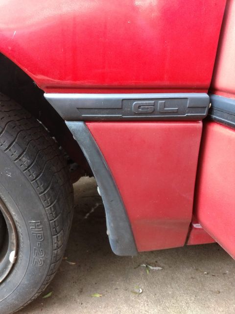 1989 Ford Probe - A close-up view of the rear fender area of a red car, showing a black trim piece with "GL" badging. A portion of the tire is also visible.