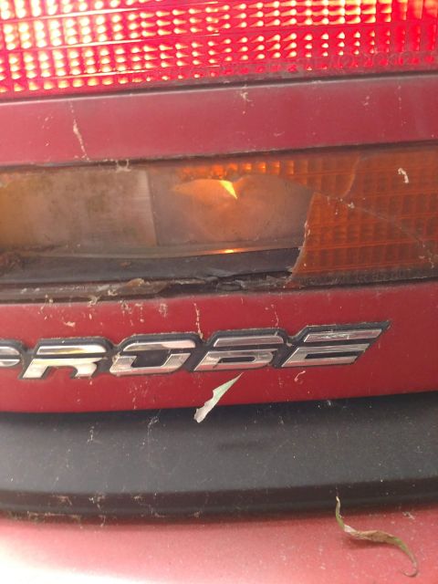 1989 Ford Probe - The 'PROBE' emblem is visible on the rear of a red vehicle, near a damaged taillight assembly.