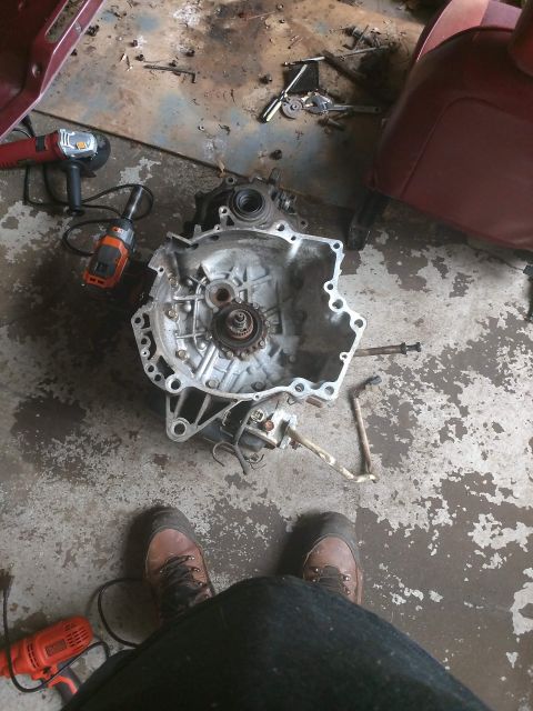 1989 Ford Probe - A disassembled transmission sits on a garage floor surrounded by tools and a car seat, indicating repair work in progress.