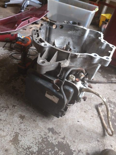 1989 Ford Probe - A transmission part is shown on a concrete floor, with tools and other items in the background. The part has hoses and electrical connector…