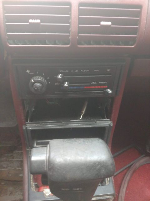 1989 Ford Probe - Interior view of a car's dashboard, highlighting the climate controls and gear shifter, with an open compartment containing a tool.