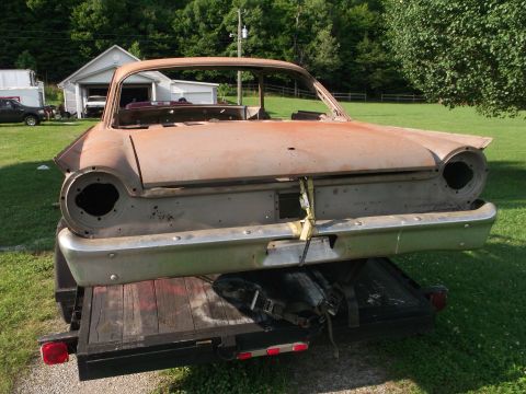 1961 Ford Starliner - This rusty car body is being transported on a trailer, showing its rear end and distinctive 1960s Ford styling.
