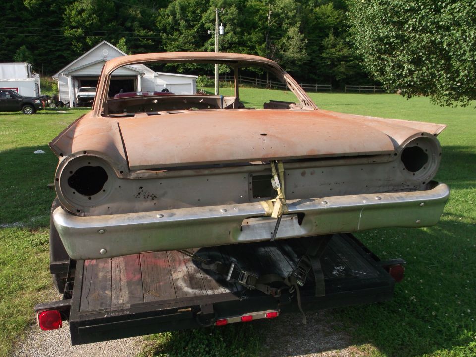 Rusty car body on a trailer, rear view. Looks like a 1960s Ford