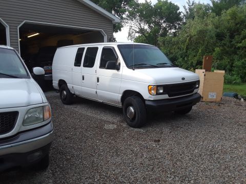 1999 Ford E250 - White 1999 Ford E250 van parked in front of a garage, with another vehicle partially visible.