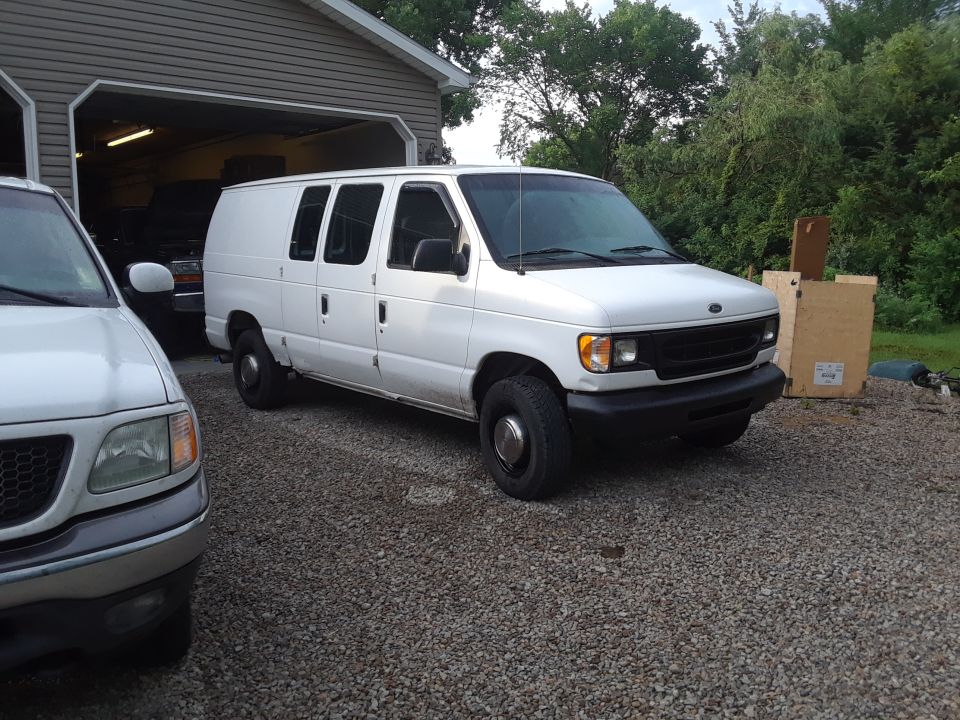 1999 Ford E250 van parked outside a garage, with the front of a pickup truck visible on the left